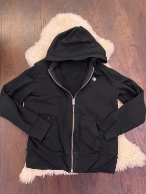 Svart hoodie från Diesel - Säljer en svart hoodie från Diesel med dragkedja framtill och två fickor. Vet inte helt säkert storleken eftersom jag inte hittade den inne i tröjan men den passar för dig som är cirka 164 Märket har en rund logga på bröstet där det står diesel. Hoodien är gjord i mjukt bomullsmaterial och har en klassisk passform med huva. Kom dm för prosförslag frågor elelr bilder. Säljer riktigt billigt som vanligt så passa på!