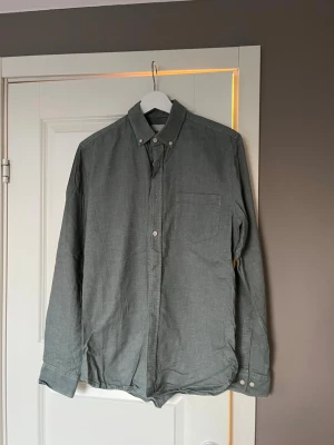 Grön skjorta med knappar från Dobber - Stilren grön skjorta från Dobber med klassisk krage och knappar framtill. Skjortan har en bröstficka och långa ärmar med knapp vid manschetten. Perfekt till jeans eller chinos för en clean look. Slim fit