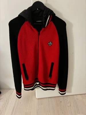 Röd och svart cardigan från J.Lindeberg - Snygg cardigan från J.Lindeberg i rött och svart. Skick 8/10, två mindre defekter i fickorna på sidorna, två mindre hål. Storlek S. För fler bilder eller frågor kom dm. Priset kan diskuteras.