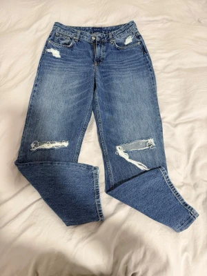 Blå slitna jeans från Gant - Ett par blå Gant jeans med raka ben och flera slitningar på både fram- och baksida. Jeansen har klassisk femficksdesign, hög midja och är gjorda i kraftig denim. Perfekta för en avslappnad och trendig look.