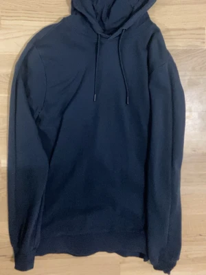 Mörkblå hoodie från Hummel - Klassisk mörkblå hoodie från Hummel med justerbar dragsko i huvan och ribbade muddar. Perfekt för chill dagar eller när du vill ha en enkel och stilren look. Tillverkad i mjuk bomull för skön känsla.