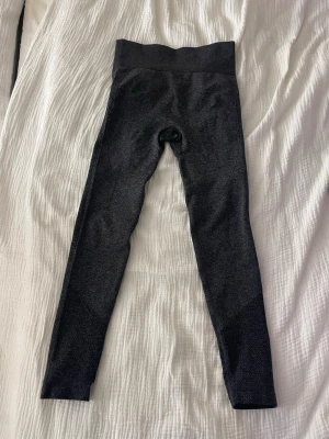 Träningstights - Säljer ett par svartgråa tränings tights. De är stretchiga och har en diskret struktur i materialet, perfekta för träning eller chill. Inga synliga loggor eller fickor. Passar dig som gillar stilrena och bekväma tights.