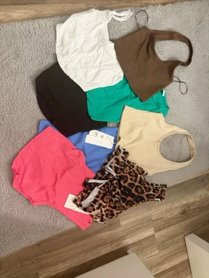 Mix av trendiga ribbade linne-toppar - Säljer ett paket med åtta linne-toppar i olika färger och mönster. Färgerna är vit, brun, svart, grön, blå, beige, rosa och ett leopardmönstrat. De flesta är ribbade och har ärmlös design med croppad passform. Perfekta för att mixa och matcha till olika outfits! Kan även säljas styckvis🤍