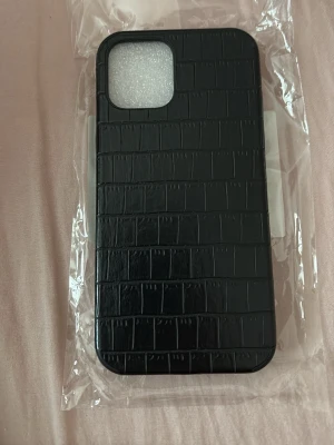 Svart mobilskal med krokodilmönster - Stilrent svart mobilskal med krokodilmönstrad yta som ger ett lyxigt intryck. Skalet är tillverkat i ett glansigt material som känns både tåligt och snyggt. Passar perfekt för dig som vill ha ett unikt och trendigt skydd till din mobil.