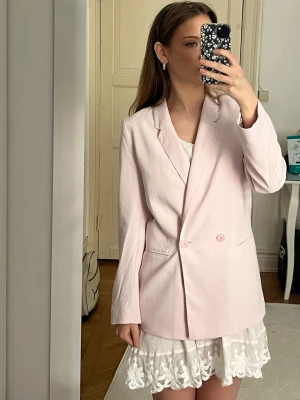 Ljusrosa oversized kavaj - Säljer en ljusrosa oversized kavaj med klassisk krage och två knappar framtill. Kavajen har raka ärmar och två fickor på sidorna. Perfekt för dig som gillar en trendig och avslappnad look. Går att klä upp och ned, matcha med jeans till kjol! 