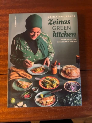 Zeinas Green Kitchen kokbok - Säljer kokboken 'Zeinas Green Kitchen' av Zeina Mourtada. Boken har ett färgstarkt omslag med matbilder och grön text. Innehåller gröna recept från olika delar av världen, med fokus på vegetariska och veganska rätter. Perfekt för dig som vill utforska nya smaker.