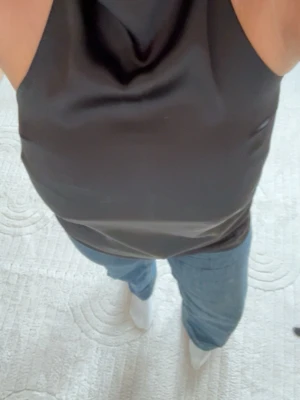 Svart halterneck topp i satin - Säljer en svart halterneck topp i satin med hög hals och ärmlös design. Toppens material har en snygg glans och sitter tight över kroppen. Perfekt för dig som vill ha en stilren och trendig look. Nypris : 450kr