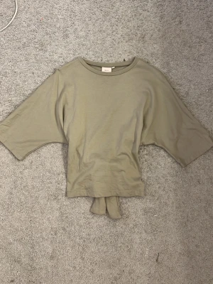 Grön topp från Nelly - Snygg grön topp från Nelly med vida korta ärmar och knyt i ryggen. Perfekt till jeans eller kjol för en chill och trendig look. Tillverkad i mjuk bomull som känns skön mot huden.