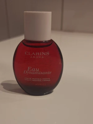Clarins Eau Dynamisante parfym 15 ml - Clarins Eau Dynamisante är en parfym i en snygg röd glasflaska på 15 ml. Doften kombinerar fräschör och vitalitet med en hint av växtextrakt. Perfekt för dig som gillar energigivande och fräscha dofter. Helt oanvänd, pris kan diskuteras 🫶