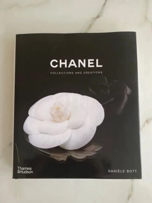 Chanel Collections and Creations bok - Säljer en snygg coffee table-bok 'Chanel Collections and Creations' av Danièle Bott. Boken har ett elegant svart omslag med en vit kameliablomma och innehåller inspirerande bilder och texter om Chanels mode och parfym. Perfekt för modeintresserade.