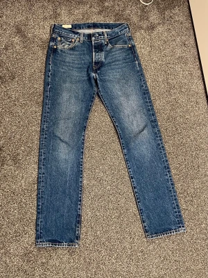 Levi’s 501 Jeans – Blå, W30 L32  - Klassiska blå Levi’s 501 med rak passform och fem fickor. Tidlös tvätt i slitstark denim, med ikonisk läderpatch bak i midjan och röda Levi’s-taggen på bakfickan.  Perfekta för en avslappnad och stilren look. Använda endast 2 gånger – nästan som nya!  Storlek: W30 L32 Pris: 439 kr Skick: Nästan som nya