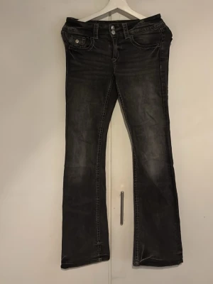 Svarta bootcut jeans med slitningar - Säljer ett par svarta bootcut jeans med snygga slitningar och kontrastsömmar. Jeansen har fem fickor, låg midja och stängs med knapp och dragkedja. Perfekta för en avslappnad och trendig look.