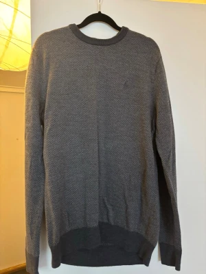 Mörkgrå stickad Ralph Lauren - Snygg mörkgrå stickad tröja med diskret fiskbensmönster. Tröjan har rund halsringning och ribbade muddar vid ärmslut och nederkant. Perfekt för dig som gillar stilrena och klassiska plagg. Passar L