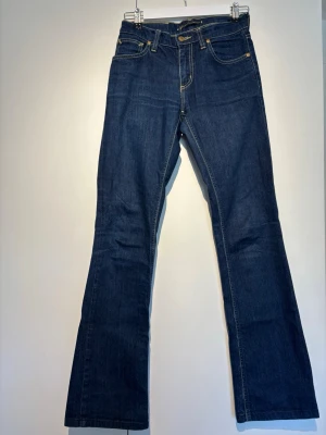 Mörkblå bootcut jeans  - Säljer ett par mörkblå bootcut jeans med klassiska fem fickor och kontrastsömmar. Jeansen har normal midja och är tillverkade i slitstark denim. Perfekta för dig som gillar en tidlös och avslappnad stil.
