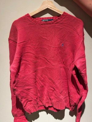 Röd stickad tröja Polo Ralph Lauren - Snygg röd stickad tröja från Polo Ralph Lauren med rund halsringning och diskret logga broderad på bröstet. Tröjan har ribbade muddar vid ärmslut och nederkant, perfekt för en avslappnad men stilren look.