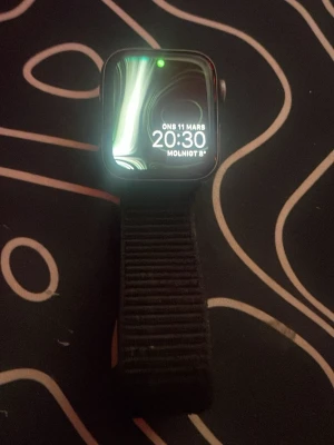 Apple Watch Series 4 44mm svart - Apple Watch Series 4 med 44mm boett i svart aluminium och svart sportband. Klockan har en fyrkantig form, digital krona och pulssensor på baksidan. Perfekt för att hålla koll på träning, notiser och hälsa direkt på handleden.