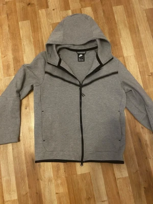 Nike tech - Säljer denna Nike tech fleece. Den är i storlek m och har en liten fläck vid luvan. Den har två inne fickor och en ficka med zip på vänstra armen. Har inte använts mycket. Den har legat i garderoben oanvänd och sedan hade jag på mig den några gånger nyss. Skriv om ni är intresserade. 