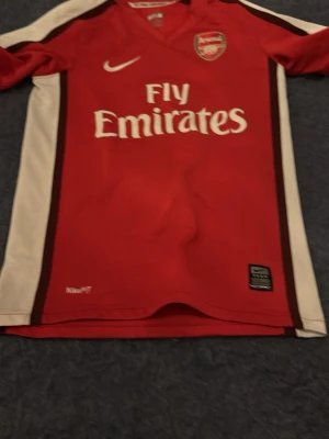 Arsenal matchtröja retro - Snygg Arsenal matchtröja från Nike i rött med vita ärmar och bruna detaljer. Tröjan har Fly Emirates-tryck på bröstet, Arsenal-logga och nummer 10 med Gallas på ryggen. Tillverkad i lätt och ventilerande material, perfekt för fotboll eller träning. Pris är diskuterbart. 