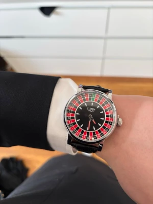 Svart roulette-klocka  - Säljer en unik klocka med en cool urtavla inspirerad av ett roulettehjul. Den svarta urtavlan med röda, svarta och gröna detaljer gör klockan väldigt iögonfallande och perfekt för dig som vill ha något annorlunda.