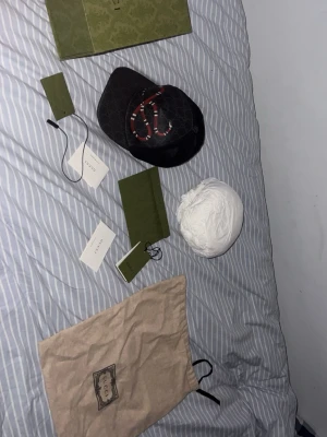 Svart Gucci keps med ormtryck - Säljer en svart keps från Gucci med det klassiska GG-mönstret och en röd orm broderad framtill. Kepsen har böjd skärm och mesh på baksidan för extra ventilation. Märkesetiketter och dustbag medföljer. Perfekt för dig som vill ha en statement-accessoar.