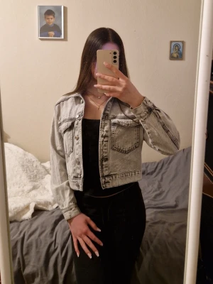 Ljusgrå jeansjacka från Gina Tricot - Snygg ljusgrå jeansjacka från Gina Tricot med klassisk krage, knappar framtill och två bröstfickor. Jackan har en croppad passform och markerade sömmar som ger en cool vintagekänsla. Perfekt att slänga över en hoodie eller t-shirt.