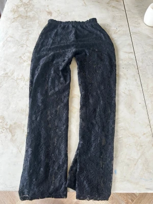 Svarta spetsleggings med vida ben - Säljer ett par sv NBarta leggings i spets med vida ben och elastisk midja. De har ett genombrutet blommönster pipeline hellängd och är mural stretchiga. Perfekta för dig som vill ha något extra till outfiten. Materialet känns lätt och luftigt.