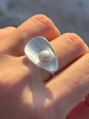 Modern silverring med pärla - Unik och trendig silverring med en vit pärla i mitten. Ringen har en asymmetrisk, triangelformad topp och är justerbar för att passa olika storlekar. Perfekt för dig som gillar stilrena och moderna accessoarer med en twist.