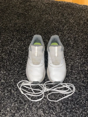 Golfskor Puma  - Säljer ett par vita sneakers från Puma med klassisk låg profil. Skorna är i läder med meshdetaljer på ovandelen och har grå insida samt vita skosnören. Puma-loggan syns på sidan. Perfekta för en clean och sportig look.