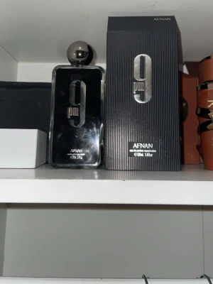 Afnan 9PM Eau de Parfum 100ml - Afnan 9PM Eau de Parfum är en elegant parfym i en svart, rektangulär flaska med metallisk silverdetalj och rund kork. Flaskan rymmer 100 ml och kommer i en matchande svart förpackning med stilren design. Perfekt för dig som gillar moderna och intensiva dofter.