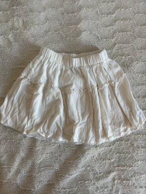 Vit volangkjol  - Söt vit kjol med volangdetaljer och resår i midjan. Kjolen har en lätt och luftig känsla, perfekt för varmare dagar. 