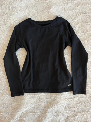 Svart långärmad träningströja - Snygg svart träningströja från Intersport. Fint tryck på ryggen och ett litet märke på framsidan vid kanten, i storlek 110/116. Säljer den för den har blivit för liten. 