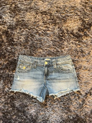 Blå y2k jeansshorts med fransig kant - Från Gina Tricot: Snygga blå jeansshorts med fransig, rå kant och slitna detaljer. Y2k modell med guldfärgade knappar och bälteshällor. Perfekta för sommaren och våren. Strlk 152. Använda 2 gngr de är nu för små för mig. ALLA PRISER KAN DISKUTERAS🤍