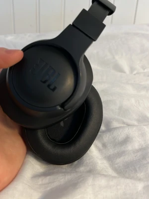 Svarta over-ear hörlurar från JBL - Snygga svarta over-ear hörlurar från JBL med mjuka, vadderade kåpor och justerbart huvudband. Tillverkade i plast och konstläder för en bekväm känsla och stilren look. Perfekta för att lyssna på musik eller poddar när du är på språng.