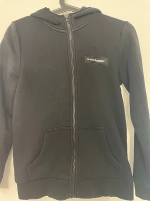 Svart hoodie från Peak Performance - Svart hoodie med dragkedja från Peak Performance. Klassisk design med huva, två stora fickor framtill och logotyp på bröstet. Tillverkad i mjukt material som passar perfekt till en avslappnad stil.