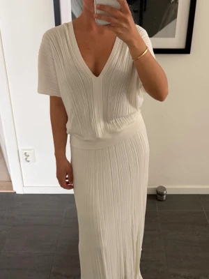 Vit plisserad Zara set - strl 38 i kjol och strl 36 i topp - Snygg vit långklänning med plisserat tyg och v-ringning. Klänningen har korta ärmar och markerad midja för en smickrande siluett. Perfekt för sommarens alla tillfällen och enkel att styla med accessoarer. Setet funkar för mig som bär 34/36. Liten fläck på toppen