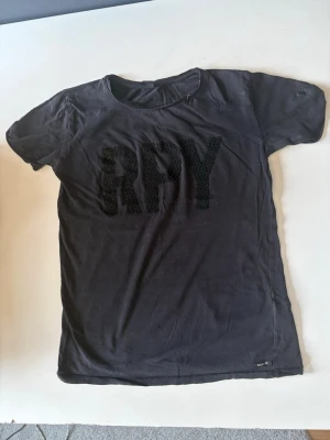 Svart T-shirt från Replay - Svart t-shirt från Replay med stort RPY-tryck framtill i en textur som sticker ut. Klassisk rund halsringning och korta ärmar. Perfekt för en avslappnad och cool stil.