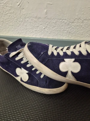 Mörkblå/Navy sneakers från The Gallerist. Skriv till mig om pris, kan diskuteras - Säljer ett par mörkblå sneakers från The Gallerist med vit sula och vita skosnören. Skorna har en unik vit klöverdetalj på sidan och är gjorda i mocka. Perfekta för dig som vill sticka ut med en cool och annorlunda look.