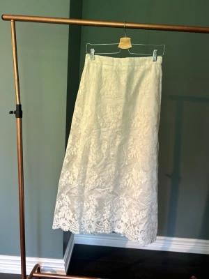 Vit långkjol med spetsdetaljer från Culture  - Säljer en elegant vit långkjol med vackra spetsdetaljer och blommigt mönster. Kjolen har en rak passform och är perfekt för dig som gillar en romantisk och stilren look. Materialet känns lätt och flowy, perfekt för varmare dagar. Ny med prislapp, nypris: 1000kr.  Storlek S