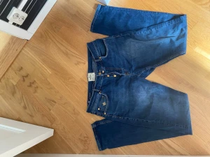 Morris Steve Satin Jeans blå 34/34 - Snygga blå jeans från Morris, modell Steve Satin Jeans. Klassisk femficksdesign med guldfärgade knappar och broderad detalj på fickan. Jeansen har raka ben och är tillverkade i ett mjukt denimtyg som känns bekvämt hela dagen.