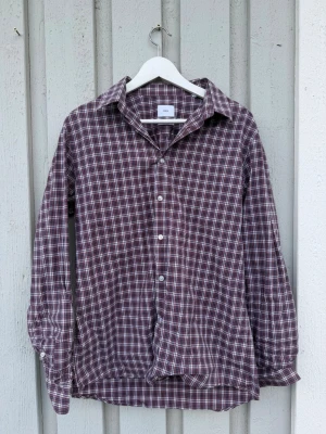 Rutig skjorta från Bläck - Rutig skjorta från Bläck i vinröda, vita och blå toner. Skjortan har lång ärm, klassisk krage och knäppning framtill. Modellen är tailored fit och passar perfekt till en avslappnad men ändå stilren look. TITTA ÄVEN MINA ANDRA SKJORTOR I MIN PROFIL!🥳🤝