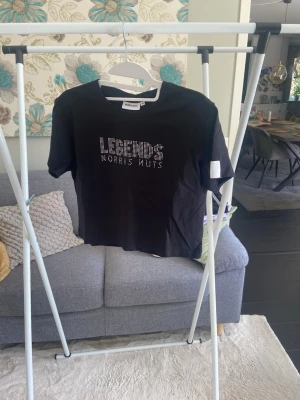 Svart t-shirt Norris Nuts Legends - Svart t-shirt från Norris Nuts med texten 'LEGENDS' i glittriga stenar på bröstet. Modellen är kortärmad och har en klassisk passform. Perfekt för dig som gillar streetstyle och vill sticka ut med coola detaljer. En exklusive produkt som inte säljs längre, den är aldrig använd och alla stenar är på plats. Ursprungspriset är 400kr. Liten i storleken så M känns som S/XS