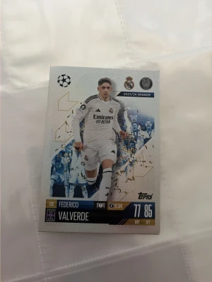 Topps fotbollskort Federico Valverde - Samlarfotbollskort med Federico Valverde från Real Madrid, Champions League 2023/24 Winner. Kortet har vit och blå design med guldiga detaljer och visar spelaren i matchställ. Perfekt för dig som gillar fotboll och samlarkort.