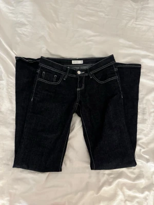 Low waist bootcut jeans - Snygga mörkblå jeans från Gina Tricot med vita kontrastsömmar och klassisk femficksdesign. Jeansen är bootcut och låg midja. Perfekta för dig som gillar en stilren look. Dom är använda max 3 ggr