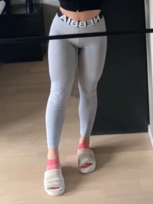 Grå leggings från Nebbia - Snygga grå leggings från Nebbia med mid-rase midja och bred resår med logga. De är tighta och följsamma, perfekta för träning eller chill. Materialet är stretchigt och mjukt för maximal komfort.