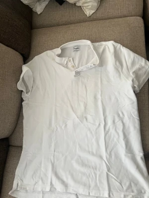 Vit slim fit t-shirt med knappar - Säljer en vit slim fit t-shirt från C med korta ärmar och knappdetaljer vid halsen. T-shirten har en enkel och clean look, perfekt för dig som gillar stilrena plagg. Tillverkad i mjuk bomull för skön känsla hela dagen.