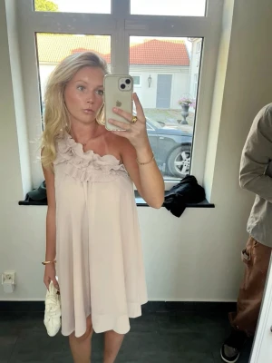 Ljusrosa one shoulder klänning med volang - Superfin ljusrosa klänning med one shoulder och flera lager plisserade volanger upptill. Klänningen har en luftig och kort modell som ger en romantisk vibe. Perfekt för sommarens alla tillfällen!