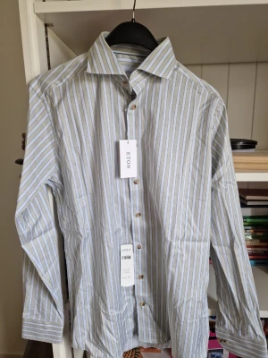 Randig skjorta från Eton, slim fit - Snygg randig skjorta från Eton i slim fit-modell. Skjortan har blå, vita och beige ränder, klassisk krage och knäppning framtill. Perfekt för dig som gillar stilrena och fräscha skjortor med modern passform.