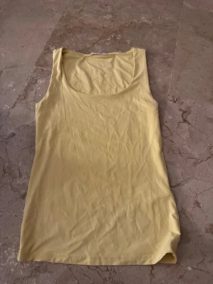 Gul ärmlös linnetopp - Snygg gul linnetopp med rund halsringning och ärmlös design. Perfekt för varma dagar och enkel att matcha med jeans eller kjol. Mjuk och skön känsla tack vare bomullsmaterialet.