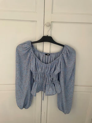 Blå blommig blus med puffärmar - Supersöt blå blus från bikbok med små blommor, puffiga långa ärmar och midja med snörning. Den är knappt använd och passar perfekt till sommaren. 