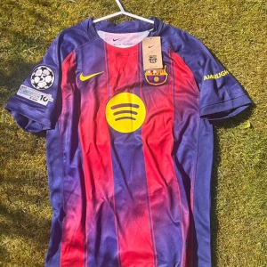 FC Barcelona matchtröja Lamine Yamal - Säljer en FC Barcelona matchtröja från Nike med Lamine Yamal och nummer 10 på ryggen. Tröjan är röd och blå med gula detaljer, klubbmärke och sponsorloggor på bröstet. Korta ärmar och Champions League-märke på ärmen. Perfekt för fotbollsfans!